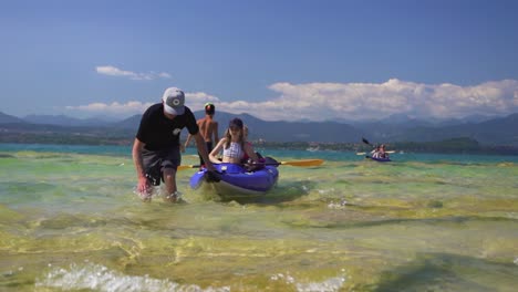 Full-shot-of-man-pulling-daughter-through-shallow-lake-water-in-a-canoe-boat,-on-Jamaica-Beach,-Sirmione,-Lago-Garda,-Lake-Garda,-Italy