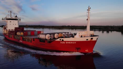 A2B-energy-vessel-in-red-sailing-through-water-channel-carrying-freight-of-shipment-container-and-tank-container-Ariel-shot-upclose