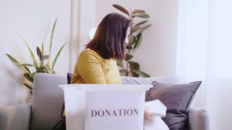 Asian-woman-selecting-clothes-for-donation-and-putting-in-box