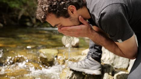 Ein-Bärtiger-Männlicher-Reisender-Wäscht-Sein-Gesicht-Mit-Gebirgsbachwasser