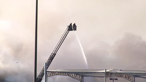 Feuerwehrleute-Sprühen-Wasser-Von-Oben-Auf-Rauchendes-Feuer