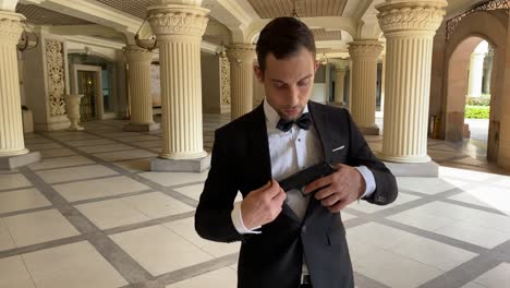 A-handsome-man-wearing-a-suit-looks-like-James-Bond-walks-straight-to-the-camera-with-a-weapon-inside-of-a-building-with-pillars