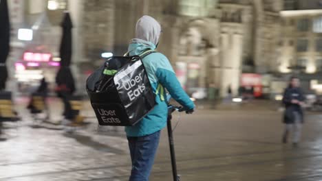 Joven-Uber-Come-Mensajero-Entregando-Comida-A-Un-Cliente-En-El-Scooter-Eléctrico-En-Invierno