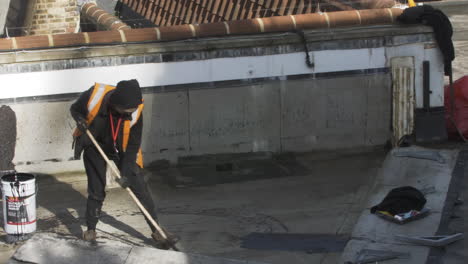 Trabajador-Masculino-Aplicando-Masilla-Bituminosa-En-El-Techo-Del-Edificio-En-Londres