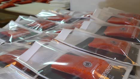 Packages-of-smoked-trout-and-salmon-stacked-on-table-with-workers-in-background---Reverse-handheld