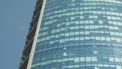 Tilt-up-of-window-cleaner-hanging-from-a-glass-curtain-wall-of-modern-skyscraper,-Santiago-Chile