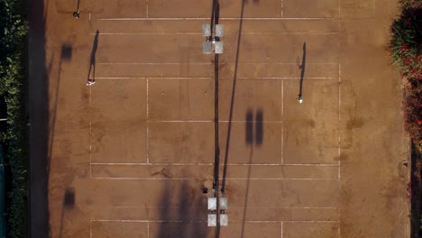 Sombras-Proyectadas-En-Una-Cancha-De-Tenis-De-Tierra-Batida-De-Una-Mujer-Joven-Y-Su-Entrenador-Durante-La-Práctica-En-La-Mañana,-Ciudad-De-México