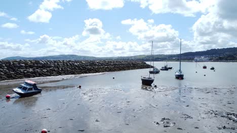 Aerial-view-moored-boats-on-Welsh-low-tide-seaside-breakwater-harbour-coastline-low-slow-orbit-right