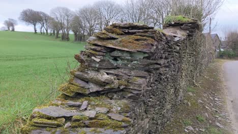 Eine-Alte-Steinmauer-In-Der-Nähe-Der-Straße-Mit-Fernblick-Auf-Das-Bauernhaus