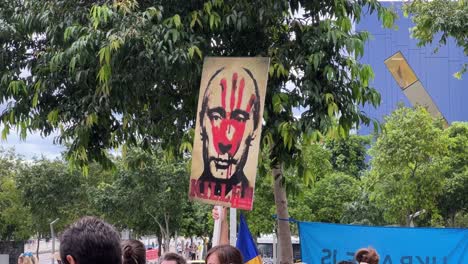 Teleobjetivo-Primer-Plano-De-Un-Cartel-Sostenido-Por-Un-Manifestante-Pacífico-En-La-Plaza-De-Brisbane-Que-Muestra-Una-Silueta-De-Mano-Ensangrentada-En-La-Cara-De-Vladimir-Putin-Expresando-Matanzas-Inhumanas-De-Militares-Rusos