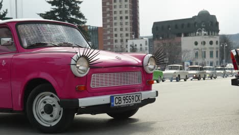 Convoy-De-Coches-Clásicos-Retro-Trabant-De-Europa-Del-Este-Conducen-Por-Las-Calles-De-La-Ciudad,-Coche-Rosa-Colorido