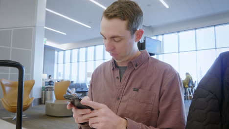 Close-up-view-of-a-male-millennial-professional-holding-a-modern-smartphone-texting-message-while-at-the-food-court-in-the-airport-close-to-San-Francisco,-California,-United-States