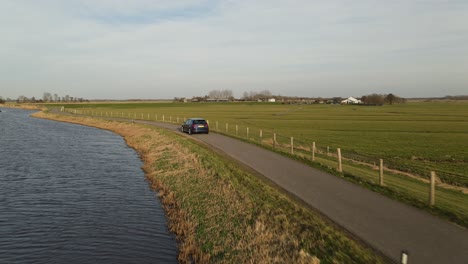 Close-up-aerial-drone-chasing-modern-dark-coloured-car-through-lonely-road