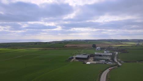 An-aerial-flight-towards-farm-buildings-and-road-with-circular-turn-over-green-fields