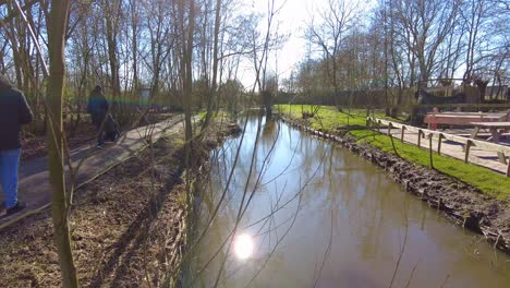 POV-Spaziergang-über-Den-Schlammigen-Fluss-Mit-Frauen,-Die-Den-Kinderwagen-Auf-Dem-Weg-Im-Fien--Und-Teun-Park-In-Groot-Ammers-Schieben