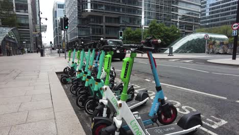 Fila-De-Scooters-Eléctricos-Sin-Muelle-Estacionados-En-Upper-Bank-Street-Fuera-De-La-Entrada-De-La-Estación-Canary-Wharf