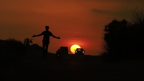 Tiefwinkelaufnahme-Eines-Mannes,-Der-Auf-Der-Straße-Mit-Blick-Auf-Den-Sonnenuntergang-Im-Hintergrund-In-Der-Stadt-Diu-In-Inida-Spazieren-Geht