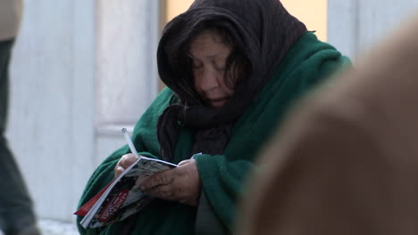 Una-Anciana-Escribe-En-Una-Revista,-Vistiendo-Una-Capa-Verde-Oscuro-Para-Protegerse-Del-Frío