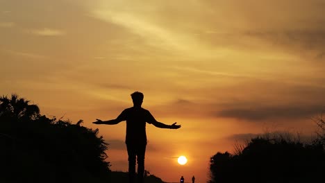 Free-silhouette-man-walking-on-the-road-among-the-mountains,-clouds,-backlit-at-sunset-at-Diu-city-of-India