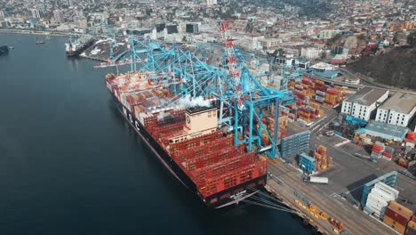 Luftumlaufbahn-Eines-Containerfrachtschiffs,-Das-In-Der-Nähe-Von-Kränen-Angedockt-Ist,-Dampf-In-Der-Luft,-Bereit-Zum-Verladen-Im-Seehafen-Von-Valparaiso,-Chile