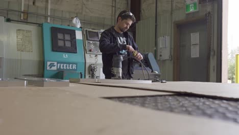 Hombre-Enchufando-El-Enrutador,-Poniéndose-Gafas-De-Seguridad-Y-Enrutando-Aluminio-En-El-Taller