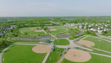 Volando-Sobre-Diamantes-De-Béisbol,-Tiro-Aéreo-De-Drones-De-Campos-De-Béisbol-Verdes-Brillantes-En-Un-Día-Soleado