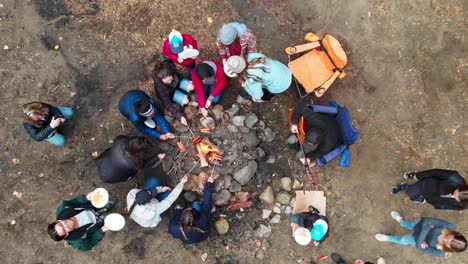 Establishing-aerial-view-of-young-people-around-campfire-roasting-hot-dogs-over-open-flame-in-the-forest