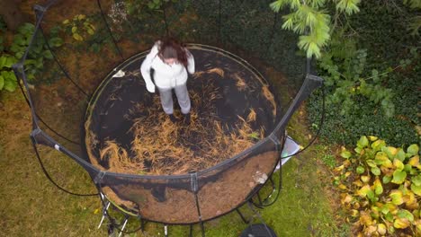 Eine-Herablassende-Drohne-Schoss-über-Ein-Junges-Mädchen,-Das-Im-Herbst-Auf-Einem-Trampolin-Sprang