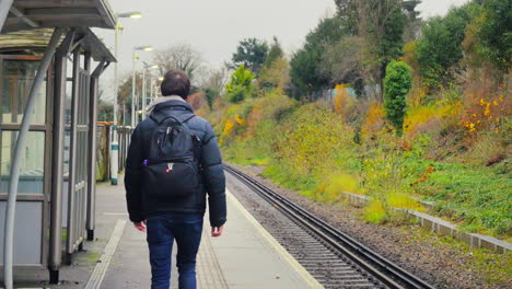 Hombre-Joven-Caminando-Sobre-Una-Plataforma-De-Estación-De-Tren-Vacía-Vista-Desde-Atrás