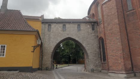 Slow-motion-shot-of-two-people-walking-under-The-Absalon-Arch-between-Roskilde-Cathedral-and-the-Museum-of-Contemporary-Art-in-Roskilde,-Denmark