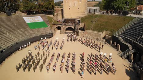 Luftdrohnenaufnahme,-Die-Um-Die-Arena-In-Avenches-(Schweiz)-Kreist,-Mit-Musikern,-Die-In-Formation-Herausmarschieren