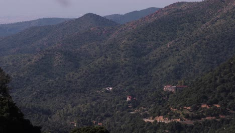 houses-in-the-middle-of-green-huge-high-mountains-with-small-car-curvy-road-in-outside-Cagliari-city-in-Sardinia,-Italy