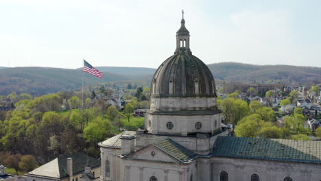 Luftdrohnenansicht-Der-Kathedrale-Des-Allerheiligsten-In-Altoona,-Pennsylvania,-Mit-Der-Amerikanischen-Flagge-Dahinter