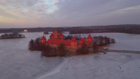 Antena:-Toma-Giratoria-Del-Castillo-De-La-Isla-De-Trakai-Con-Un-Camino-De-Puente-Sobre-Un-Lago-Congelado-Con-Gente-Patinando-Sobre-Hielo