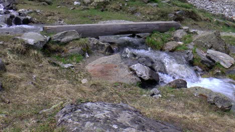 A-man-and-a-woman-walk-from-left-to-right-across-a-beam-that-serves-as-a-crossroad-over-a-waterfall