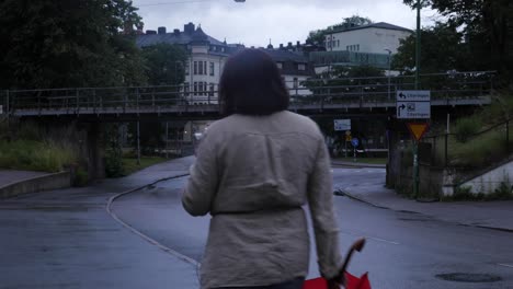 Mujer-Con-Chaqueta-Beige-Caminando-Con-Un-Paraguas-Y-Su-Teléfono-En-La-Mano-Hacia-La-Ciudad-Lluviosa-Borås