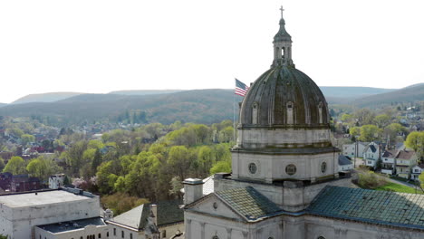 Aerial-drone-view-of-the-Cathedral-of-the-Blessed-Sacrament-in-Altoona,-Pennsylvania-with-the-American-flag-seen-behind