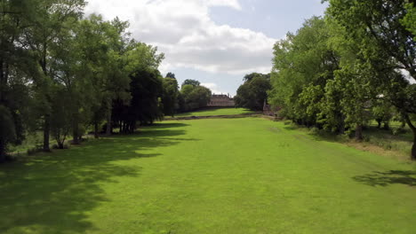 Luftaufnahme-Eines-Herrenhauses-Auf-Dem-Land,-Eingebettet-In-Einer-Von-Bäumen-Gesäumten-Allee-In-England,-Großbritannien,-An-Einem-Sonnigen-Sommertag,-Das-Sich-Zum-Haus-Hin-Neigt