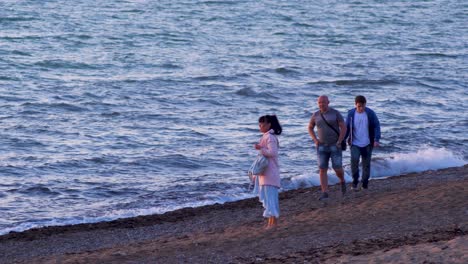 Happy-family-enjoying-romantic-sunset-at-calm-sea,-wide-shot-from-a-distance