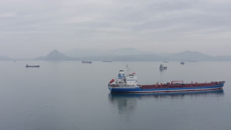 Barcos-En-El-área-De-Espera-De-Anclaje-En-Un-Clima-Tranquilo,-Con-Una-Cresta-De-Montaña-A-Lo-Lejos-En-El-Día-Nublado