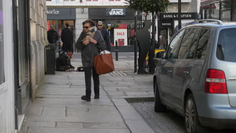 Un-Vagabundo-Sentado-En-Una-Acera-En-El-Centro-De-La-Ciudad-De-Truro-Siendo-Ignorado-Por-Los-Transeúntes,-A-Cámara-Lenta