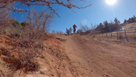 Chico-Salta-Una-Colina-En-Una-Pista-De-Tierra,-Usando-Una-Bicicleta-Todo-Terreno,-En-El-Espacio-Abierto-De-Rocas-Rojas-En-Colorado-Springs,-Colorado