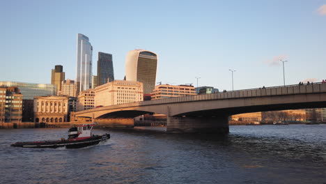 Frachtschiff,-Das-Unter-Einer-Brücke-Mit-Der-Skyline-Von-Firmengebäuden-Aus-Glas-Hindurchfährt