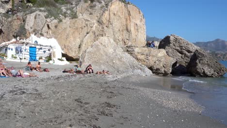 Turistas-Tomando-El-Sol-En-La-Orilla-Arenosa-De-La-Playa-De-Calahonda-En-Nerja,-Málaga,-España-Con-Olas-Marinas-Salpicando---Toma-Panorámica