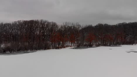 drone-aerial-over-a-frozen-lake-in-winter-in-a-forest-with-snow-4k