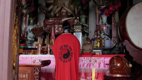 Una-Monja-Taoísta-Vestida-Con-Una-Túnica-Roja-Con-El-Símbolo-Yin-yang-En-El-Altar-Cubierta-Con-Tela-Rosa-Y-Roja---Alejamiento-Amplio