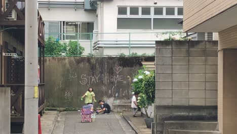 Niños-Japoneses-Jugando-Junto-A-Una-Pared-Con-Quedarse-En-Casa-Escrito-Durante-La-Pandemia-De-Coronavirus-En-Kyoto,-Japón