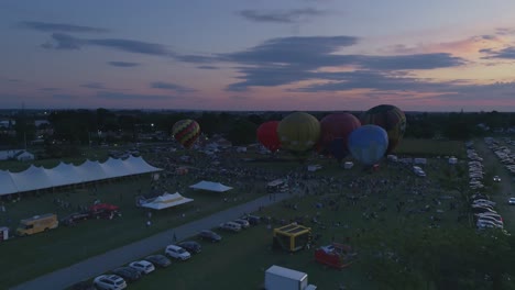 Luftaufnahme-Von-Heißluftballons,-Die-Sich-Für-Eine-Nächtliche-Flammenshow-Bei-Einem-Ballonfestival-Bei-Sonnenuntergang-Füllen,-Wie-Von-Einer-Drohne-Gesehen