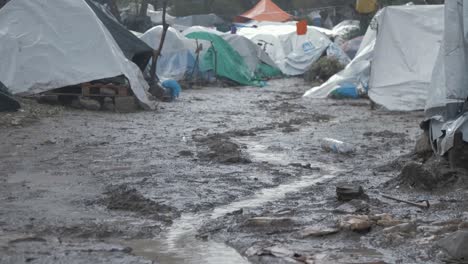 Tiro-De-ángulo-Bajo-Sombrío-Campamento-De-Refugiados-De-Moria-Tiendas-De-Campaña-En-Condiciones-Fangosas-E-Inhumanas,-Rack-Focus-Child-Blue-Poncho