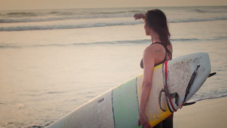 Professionelle-Surferin-Beobachtet-Selbstbewusst-Den-Sonnenuntergang-Und-Hält-Ein-Surfbrett-Am-Strand